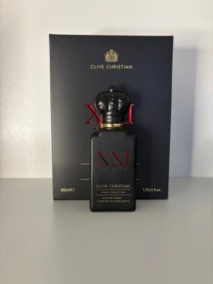 Clive Christian sampel - Lyxig parfymflaska från Clive Christian, modell XXI Art Deco ur Noble Collection. Flaskan är matt svart med röda och gyllene detaljer samt en unik kronformad kork. Volymen är 50 ml och doften heter Blonde Amber.