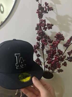 Svart LA Dodgers keps New Era - Snygg svart keps från New Era med LA Dodgers-logga broderad i vitt framtill. Klassisk 59FIFTY-modell med rak skärm och MLB-logga bak. Tillverkad i ett slitstarkt tyg som ger en clean och sportig look.