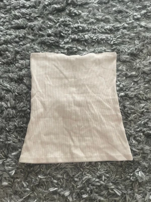 Beige ribbad tubtopp från H&M - Säljer en beige ribbad tubtopp från H&M i storlek S. Toppen är axelbandslös och har en enkel, stilren design som passar perfekt till sommaren. Materialet är mjukt och stretchigt för en bekväm passform.