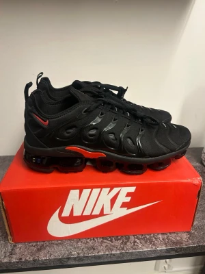 Nike Air Max varpormax - Nike Air Max vapormax i helsvart med röda detaljer och synlig Air-sula. Ovandelen är i mesh och syntet med vågiga TPU-detaljer. Klassisk Nike-logga på sidan och tungan. Skorna har en chunky sula och sportig look som sticker ut.