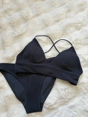 Mörkblå bikini  - Mörkblå bikini med ribbad struktur och smala axelband som korsas i ryggen. Lappen är borta men skulle gissa på att den är i storlek 34/36, xs-s
