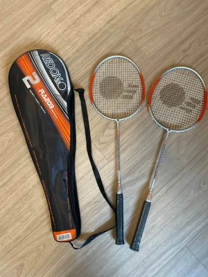 Badmintonracketar med fodral Radox - Två badmintonracketar från Radox i silver och orange med svart grepp. Racketarna kommer med ett svart och orange fodral med axelrem. Perfekt för dig som vill spela badminton med kompisar. Materialet är lättmetall och plast.