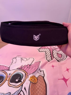 Svart sportigt pannband från AF - Konståknings Snyggt svart pannband från AF med logga framtill. Tillverkat i stretchigt material som sitter bekvämt runt huvudet. Perfekt för att hålla håret på plats under träning eller när du vill ha en sportig look.