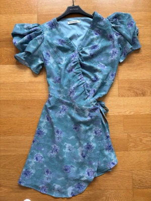 Blommig sommarklänning från Adoore - Tja säljer min mammas Adoore klänning. Endast andvänd en enda gång och har inga defekter överhuvudtaget. Inprincip helt ny! Blommigt blått lila mönster med puffiga ärmar och knyt i midjan. Det ger en trendig silloute och passar perfekt för våren och sommaren. Nypris ca 1600 kr! Tveka inte på att skriva till mig vid eventuella frågor.
