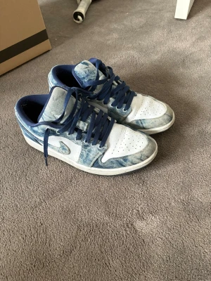 Nike Air Jordan 1 Low limited edition  - Säljer ett par Nike Air Jordan 1 Low med blått och vitt tie dye-mönster. Skorna har vita detaljer, blå snörning och klassisk swoosh på sidan. Ovandelen är i textil och läder, med perforerad tåbox för extra ventilation. Perfekt för dig som vill sticka ut.