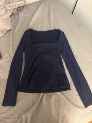 Mörkblå långärmad topp - En enkel och stilren mörkblå topp med lång ärm och fyrkantig ringning. Perfekt att matcha med jeans eller kjol för en clean look. Tillverkad i mjukt bomullsmaterial som känns skönt mot huden.
