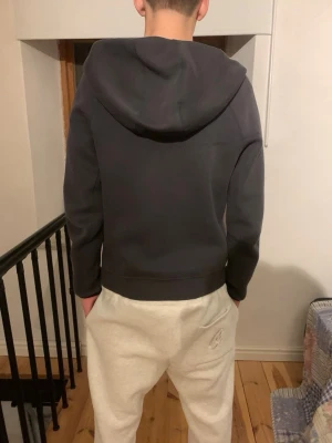 Svart Nike tech zip-hoodie från Nike - Snygg svart hoodie med dragkedja från Nike. Klassisk design med huva och diskret Nike-logga på bröstet. Mjuk och bekväm, perfekt till chill eller streetwear. Långa ärmar och ribbade muddar. Passar dig som gillar enkel och stilren look.