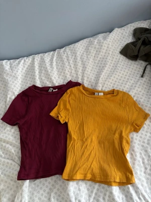 Ribbad vinröd & gul t-shirt  - Säljer två ribbade t-shirts från H&M med korta ärmar och rund hals.💛❤️T-shirten har en croppad passform och är gjord i mjuk bomull, perfekt för en avslappnad och trendig look💄
