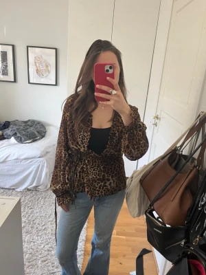 Leopardmönstrad omlottblus - Säljer en leopardmönstrad omlottblus med volangkant och knytband i midjan. Blusen har djup urringning och långa ärmar med resår och knyt vid ärmslut. Perfekt för en trendig och cool look.