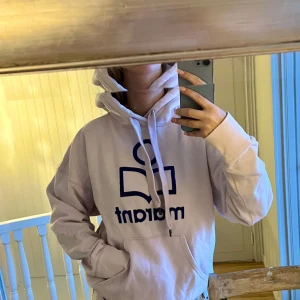 Isabel marant hoodie - Ljusrosa hoodie från Isabel Marant med stor blå logga framtill. Klassisk modell med huva, dragsnören och känguruficka. Mjuk bomullskvalitet och avslappnad passform, perfekt för en chill look. Använd med defekter som visas på bild. Nypris över 3000