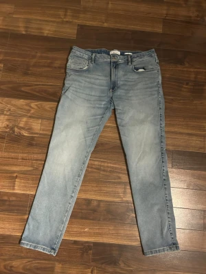 Ljusblå jeans slim - Säljer ett par ljusblå jeans med rak passform och klassisk femficksdesign. Jeansen har en något tvättad look och normal midja. Perfekta till vardagsstilen och lätta att matcha med olika plagg. Materialet är denim i bomull.