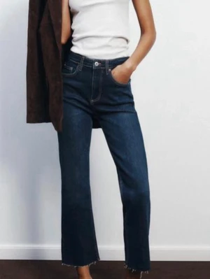 Mörkblå bootcut jeans från Zara  - Säljer ett par mörkblå bootcut jeans med hög midja, fransig kant nedtill. Jeansen har klassiska kontrastsömmar. Perfekta för en avslappnad men trendig look.