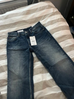 Mörkblå raka jeans från Zara - Säljer ett par mörkblå jeans från Zara med raka ben. Jeansen har snygga slitningar och tvättade detaljer framtill. Tillverkade i bomull med en bekväm passform.