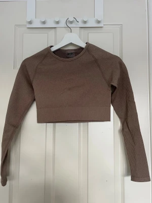 Aim'n Träningströja Espresso Ribbed - Aim'n Träningströja Espresso Ribbed. Snygg beige ribbad croppad topp med långa ärmar. Perfekt för en stilren och modern look. Toppen har en tight passform som framhäver figuren. ALDRIG ANVÄNT! Nypris på tröjan 499kr