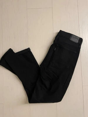 Svarta slim fit jeans från Levi's - Svarta jeans från Levi's med klassiska femficksdetaljer. Jeansen har en snygg svart läderpatch bak i midjan och är tillverkade i ett stretchigt denim-material som sitter skönt och följsamt.