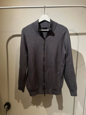 Mörkgrå ziptröja från Massimo dutti - Mörkgrå ziptröja från Massimo dutti med hög krage och två fickor framtill. Tröjan har ribbade muddar vid ärmslut och nederkant samt en stilren, minimalistisk design. Perfekt för lager på lager och enkel att matcha.