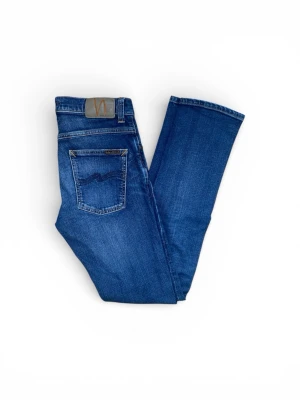 Nudie Jeans Grim Tim - Snygga blå jeans från Nudie Jeans med klassisk femficksdesign och subtila slitningar. Jeansen har normal passform och raka ben, tillverkade i mjukt bomullsdenim. Perfekta för dig som gillar stilrena och tidlösa jeans.