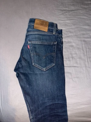 Levi's 512 selvedge - Säljer ett par klassiska blå jeans från Levi's med slim passform och fem fickor. Jeansen har snygga slitningar och en brun läderpatch bak i midjan. Perfekta för en avslappnad och stilren look.