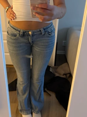 Ljusblå bootcut jeans - Säljer ett par ljusblå bootcut jeans med klassisk femficksmodell och låg midja. Jeansen har en snygg tvättad look och stängs med knapp och dragkedja. Perfekta för en avslappnad och trendig stil.