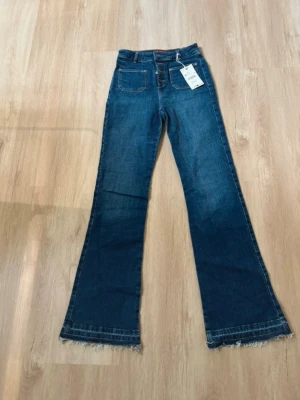 Blå utsvängda jeans från Zara - Snygga blå jeans från Zara med hög midja och utsvängda ben. Jeansen har råa kanter nertill, knappgylf och framfickor. Perfekta för dig som gillar en trendig och avslappnad stil.
