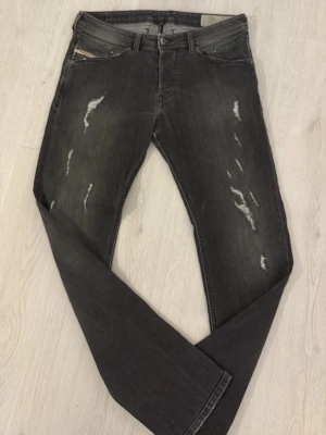 Svarta slitna jeans från Diesel - Säljer ett par svarta jeans från Diesel med slitningar och distressed detaljer framtill och baktill. Jeansen har klassisk femficksmodell, knappgylf och smal passform. Materialet är stretchigt denim för extra komfort. W32 L32 grymt snygga 