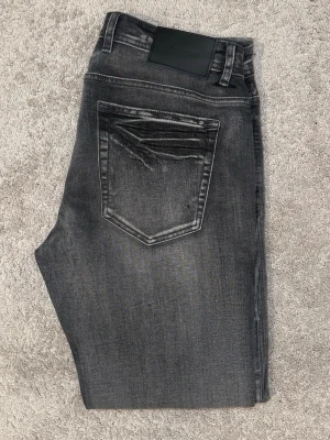 Grå slim fit jeans  - Snygga grå slim fit jeans från med slitna detaljer och tvättad look. Jeansen har klassisk femficksdesign, svarta sömmar och en svart patch bak i midjan. Perfekta för en trendig och avslappnad stil.