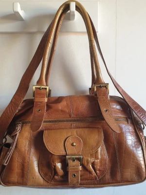 WERA Stockholm vintage läder/skinn väska brun - WERA Stockholm vintage läder/skinn väska i färgen brun/konjak färg, lädret är krokodilmönster.   Man kan ställa in banden i tre olika längder! (Se de 3 sista bilderna)   Ca 43×25×12 cm.  Får plats med väldigt mycket, har även små fack på insidan och utsidan   (Lägger upp igen pga oseriös köpare)