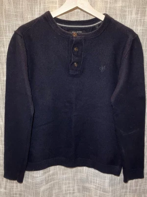 Snygg marinblå tröja från Marc O’Polo  - Mörkblå långärmad tröja från Marc O’Polo med rund halsringning och tre bruna knappar framtill. Tröjan har diskret Marc O’Polo broderad på bröstet och är tillverkad i mjukt material, perfekt för en stilren och enkel look. Oligonastorlek M aningen krympt efter tvätt, passar som storlek S( axelbredd 42cm/ längd 60cm) 
