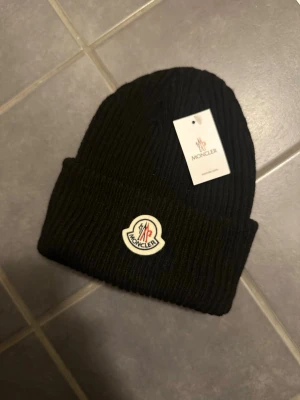 Svart Moncler Mössa - Säljer denna lite schysstare moncler mössan med etiketten fortfarande på! Ett riktigt fint pris för en fin mössa. Hör av er vid funderingar. FRAKT LÖSES SAMMA DAG/NÄSTA DAG