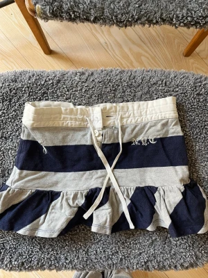 Randig volangkjol från Ralph Lauren - Kort kjol från Ralph Lauren med !inbyggda shorts! och knytband i midjan. Väldigt bra skick med en knapp som fallit av (se bild), men kjolen kan knytas med band och knäppas med de andra knapparna! Storlek S, men skulle säga att det också passar XS då den är rätt så liten. OBS köpt second hand! Hör av vid frågor, men tyvärr tar jag inte emot prisförslag så jag köpte för mycket dyrare :)