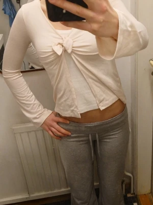 Ljusrosa topp med knyt - Snygg ljusrosa topp med lång ärm och knyt framtill. Toppen är croppad och har en enkel, stilren design som passar perfekt till jeans eller kjol. Perfekt för dig som gillar trendiga och feminina plagg.