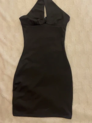 Svart halterneck kort klänning - Säljer en svart kort klänning med halterneck och snygg cut-out framtill. Klänningen har en tight passform och är perfekt för dig som vill ha en stilren och trendig look. Materialet känns mjukt och stretchigt, vilket gör den bekväm att bära hela kvällen.