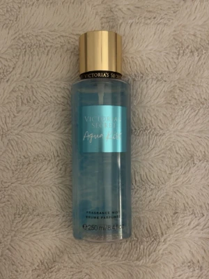 victoria secret aqua kiss - Fräsch body mist från Victoria's Secret i doften Aqua Kiss. Flaskan är cylinderformad i genomskinligt plast med blått innehåll och har en elegant guldfärgad kork. Rymmer 250 ml och har en modern, stilren design som känns lyxig och ungdomlig.