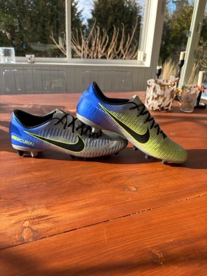 Nike Mercurial blå/gul neymar fotbollsskor - Säljer ett par Nike Mercurial fotbollsskor i en snygg blå, gul och silver färgkombination. Skorna har svarta snören, klassisk låg profil och är tillverkade i syntetmaterial för bra bollkontroll. Perfekta för dig som vill ha lätta och snabba skor på planen. *helt nya* neymar edition och har storlek 42/2 men funkar för41/2 och 42