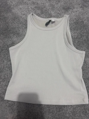 Vit ribbad linnetopp från H&M Divided - Snygg vit ribbad linnetopp från H&M Divided. Toppen är ärmlös med rund halsringning och har en tight passform. Perfekt att styla med jeans eller kjol för en fräsch look.