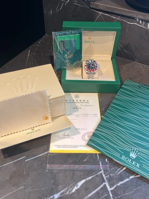 Rolex GMT-Master II Pepsi stållänk - Säljer en ikonisk Rolex GMT-Master II med den klassiska Pepsi-ringen i blått och rött. Klockan har svart urtavla, silverfärgad stållänk och levereras komplett med originalbox, certifikat och tillbehör. Perfekt för dig som gillar exklusiva accessoarer.