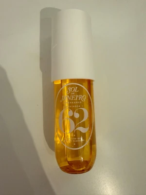 Sol de Janeiro Cheirosa 62 Parfym - Sol de Janeiro Cheirosa 62 är en ikonisk parfym i en genomskinlig, guldfärgad flaska med vit kork. Flaskan rymmer 90 ml och har en modern, rundad form. Doften är inspirerad av brasiliansk sommar och ger en varm, exotisk känsla.