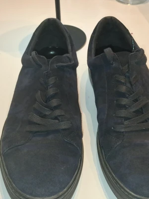 Mörkblå sneakers från J.Lindeberg - Snygga mörkblå sneakers från vagabond i mocka med klassisk snörning och låg profil. Skorna har en stilren design och passar perfekt till både jeans och chinos. Materialet är mjukt och ger en exklusiv känsla.