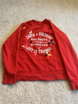 Röd sweatshirt Zadig & Voltaire - Cool röd sweatshirt från Zadig & Voltaire med tryck och broderade detaljer framtill. Texten 'Art is Truth' och färgglada stjärnor. Mjuk bomullskvalitet. !!SÄNKER MYCKET VID SNABB AFFÄR!!