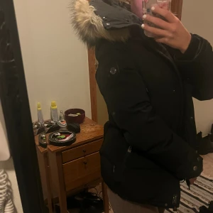 Svart Hollies dunjackajacka med päls huva - Säljer en svart dunjacka från Hollies med stor huva och fuskpälsdetalj, man kan även ta av pälsen. Perfekt för kalla dagar och har en klassisk, stilren look. Passar dig som vill ha både värme och stil. Kan skicka fler bilder privat om de behövs💕