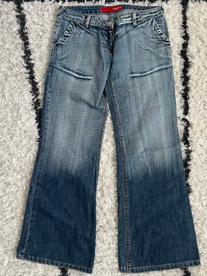 Blå jeans med slitningar - Säljer ett par blå lågmidjade raka jeans med snygga slitningar och tvättade detaljer. Jeansen har framfickor med sned öppning och breda benslut för en retro vibe. Storlek W31/L30 💙