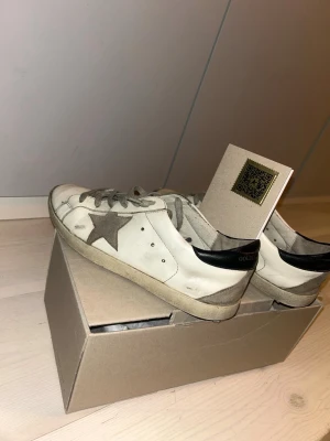 Golden Goose vita sneakers med stjärna - Golden Goose sneakers i vitt läder med grå stjärna på sidan. Lite använda, därav lite lägre pris. Låda och påse samt GG passport finns (se bild) stl 41/42