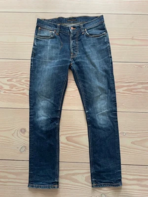 Blå jeans från Nudie Jeans - W29 L30. Bra skick förutom hål i fickorna som har försökts fixats men finns tyvärr kvar (går fortfarande att fixa). Samt lite slitage vid fickan (orangea snöret är borta) och hål vid skrevet. Modell står tyvärr inte men sitter slim. Priset är hugget i sten. Hör av er vid vidare funderingar! 😁