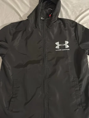 Under Armour vindjacka - Säljer en Under Armour vindjacka i storlek S men passar även folk som är 165-170cm långa , har aldrig använd jackan och den är i helt ny skick .