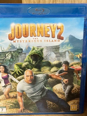 Journey 2: The Mysterious Island Blu-ray - Blu-ray-utgåva av filmen Journey 2: The Mysterious Island. Omslaget är blått med färgstarka motiv från filmen, inklusive äventyr och fantasidjur. Filmen är på engelska med svensk text och har specialfunktioner som interaktiv karta och borttagna scener.