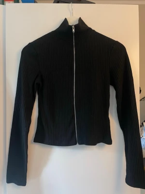 Svart och vit ribbad ziptröja - Två ribbade ziptröjor med hög krage, en svart och en vit. Båda har långa ärmar och är tillverkade i ett stretchigt material som sitter snyggt på kroppen. Perfekt för lager-på-lager och enkel att matcha med jeans eller kjol. 