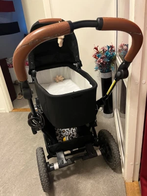 Svart barnvagn med brunt handtag - Smidig och stabil barnvagn med liggdel, perfekt för nyfödd och första tiden. LlllVagnen är lätt att köra och fungerar lika bra i stan som på grusvägar tack vare sina rejäla hjul. Finns till o med liggdel laddar upp bild på den när jag är hemma. PRIS KAN DISKUTERAS‼️‼️‼️ ✔ Rymlig liggdel med mjuk madrass ✔ Justerbart handtag i snygg brun läderlook ✔ Bra fjädring och stabil konstruktion ✔ Förvaringskorg under vagnen ✔ Lätt att fälla ihop  Vagnen är i gott skick och väl omhändertagen. Mindre slitage 