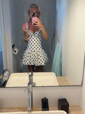 Vit prickig kortklänning med volang - ❤️!INTRESSEKOLL! ❤️Superfin vit kortklänning med svarta prickar och volang nedtill. Klänningen har en omlottliknande v-ringad front och smala axelband. Perfekt för sommarens alla tillfällen och ger en riktigt söt och trendig look. Helt ny, oanvänd storlek XS/S