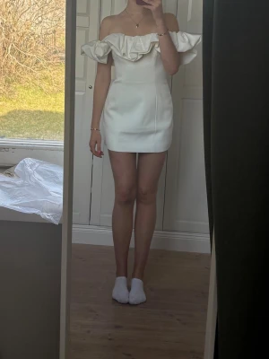 SLUTSÅLD STUDENTKLÄNNING! Vit offshoulder miniklänning med volang - Hej! Säljer en klänning jag köpte till studenten men som tyvärr är lite för kort för mig (är 182). Den är helt slutsåld och så fin verkligen men tyvärr hann jag inte skicka tillbaka innan returtiden gick ut haha. Storleken är 38 men skulle säga att det mer är en 36!  Trendig vit kortklänning med offshoulder-design och stor volang runt axlarna. Klänningen har en figurnära passform och är perfekt för dig som vill sticka ut. Materialet ser ut att vara polyester och ger en slät, elegant look.
