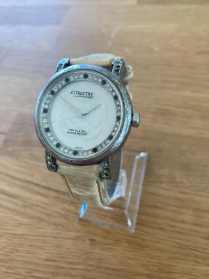 Citizen Q&Q Attractive 38mm Damklocka - Säljer en Q&Q Attractive damklocka, modell DB33J302Y. Klockan har ett silverfärgat boett med en vit urtavla och svarta detaljer. Boetten är prydd med stenar runt ramen och på bandfästena. Baksidan är i rostfritt stål och klockan är vattentålig upp till 3 BAR. Armbandet är i läder och har en ljus färg som visar tecken på användning. Skick enligt bilder, har fungerande batteri!  Nypris: 500 SEK Mitt pris: 248 SEK  Skickas alltid snabbt och spårbart. Skriv vid frågor och se gärna mina andra annonse